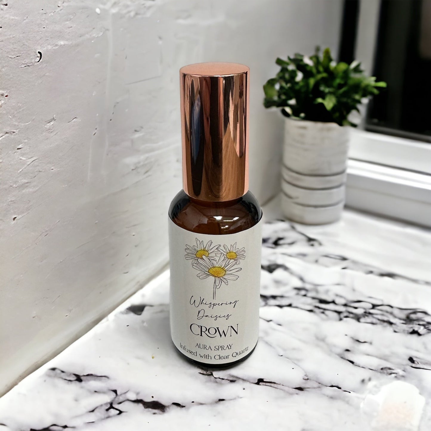 A 30ml glass bottle of 'Crown - Clear Quartz Crystal - Aura Spray' with a copper-colored cap, labeled with a sunflower design, placed on a marble surface.