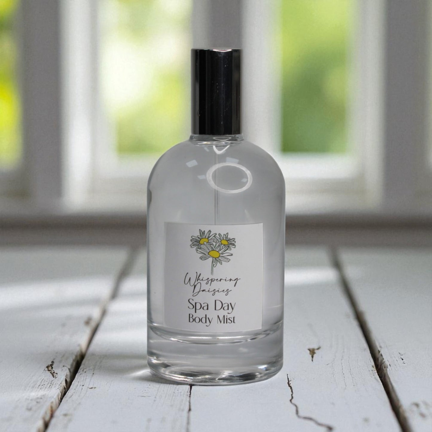 Bottle of 'Whispering Daisies Spa Day Body Mist' on a wooden surface with a blurred window background.