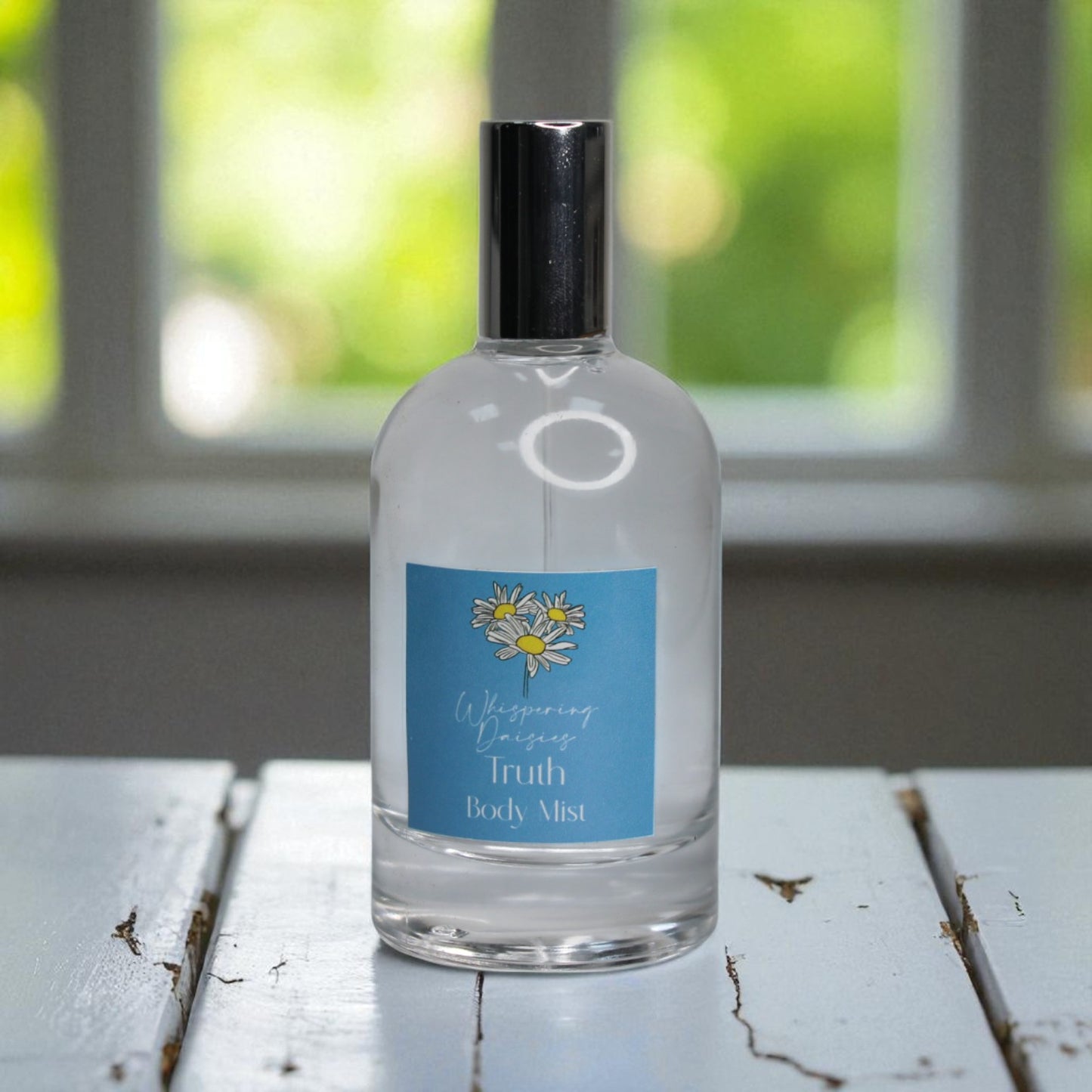 Clear bottle of 'Whispering Daisies Truth Body Mist' on a wooden surface with a blurred green background.