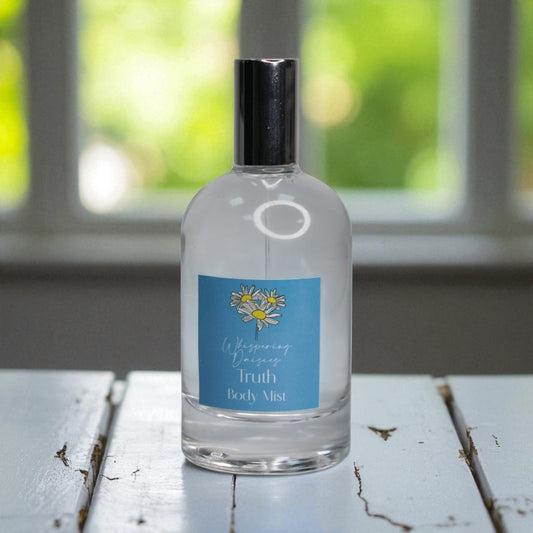 Clear bottle of 'Whispering Daisies Truth Body Mist' on a wooden surface with a blurred green background.